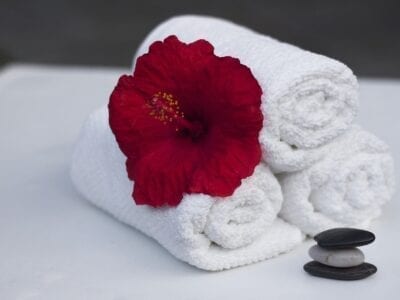 Three white hotel washcloths rolled up with a red hibiscus on them and three rocks stacked beside.