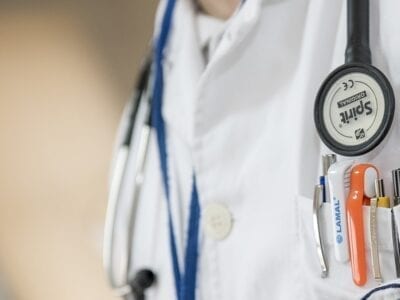 Close up photo of a doctor wearing white coat with pens in the pocket.