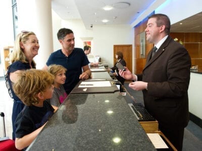 Photo of man at hotel front desk greeting a family of four.