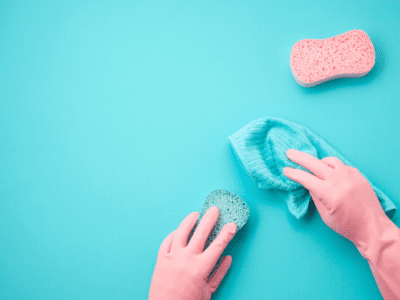 Close up photo of hands wearing pink rubber gloves using a cloth and sponge to wipe a teal surface.