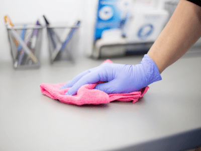 Close up photo of hand wearing purple glove and wiping counter with pink microfiber.