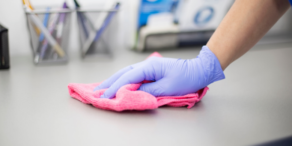 Close up photo of hand wearing purple glove and wiping counter with pink microfiber.